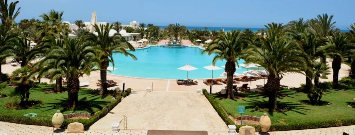 Grande piscine lagon entourée de palmiers et parasols au Royal Garden Palace à Djerba, Tunisie.