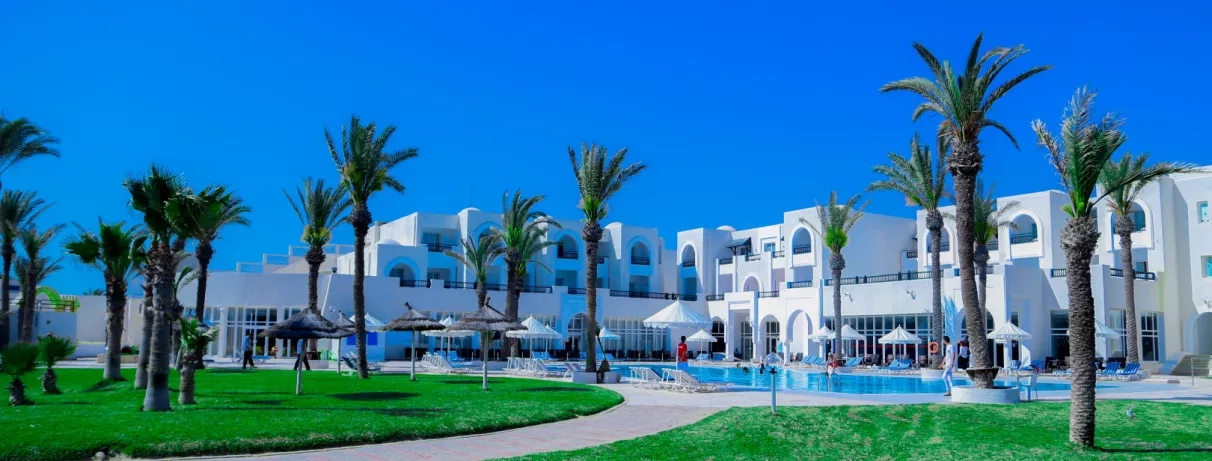 Grande piscine extérieure entourée de palmiers et architecture blanche typique de l'hôtel Al Jazira à Djerba.