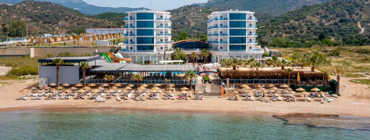 Une vue aérienne montrant l'hôtel face à une plage privée avec de nombreux parasols.