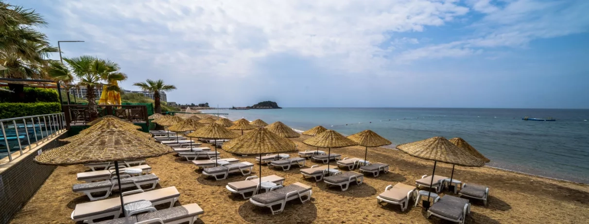 Une longue rangée de transats et de parasols en paille s'aligne le long de la plage au bord de la mer.
