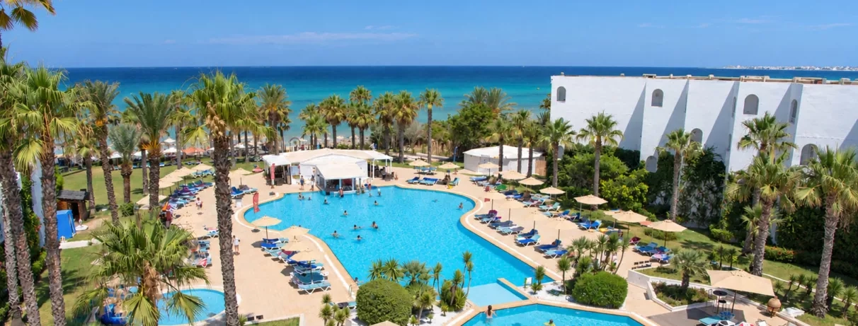 Vue aérienne de la grande piscine extérieure du Mondi Club Thalassa Mahdia entourée de palmiers avec la mer Méditerranée en arrière-plan à Mahdia en Tunisie.