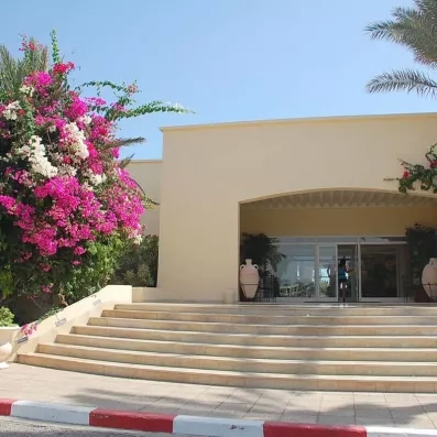 Entrée fleurie de l'hôtel Zephir à Djerba bordée de bougainvilliers roses sous un ciel bleu azur.