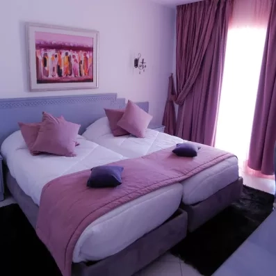 Suite confortable avec lits jumeaux, rideaux violets et tableaux d'art local à l'hôtel Al Jazira Djerba.