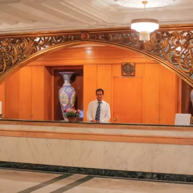Réceptionniste accueillant derrière un comptoir en marbre surmonté d'une arche sculptée dorée à l'hôtel Al Jazira.