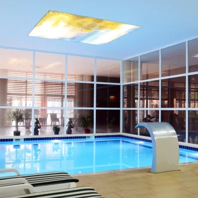 Une piscine intérieure moderne avec un plafond décoratif représentant un ciel tropical.