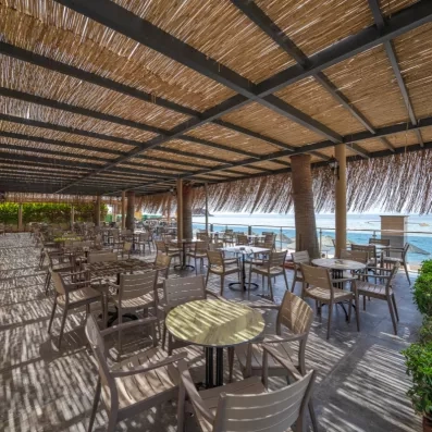 Une terrasse de café en plein air couverte d'un toit en chaume, donnant sur la plage.