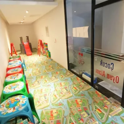Un espace de jeux intérieur pour les enfants, comprenant un tapis, des petites tables et un toboggan.