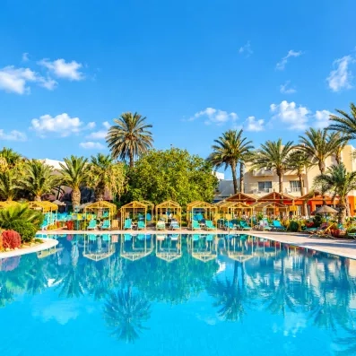 Grande piscine extérieure avec réflexions des palmiers à l'hôtel tout inclus Welcome Meridiana Djerba