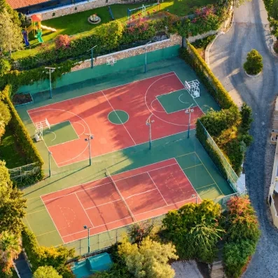 Vue aérienne de terrains de basket-ball et de tennis entourés de verdure sous une lumière dorée.