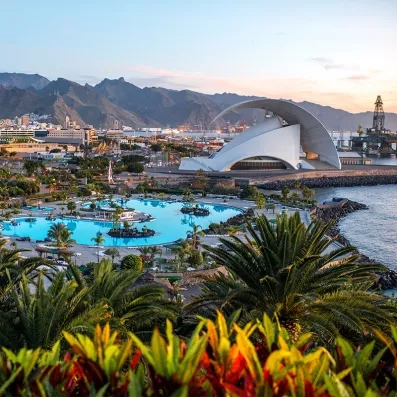 Vue de Santa Cruz de Tenerife au coucher du soleil, auditorium moderne, port, piscines maritimes et montagnes en arrière-plan.